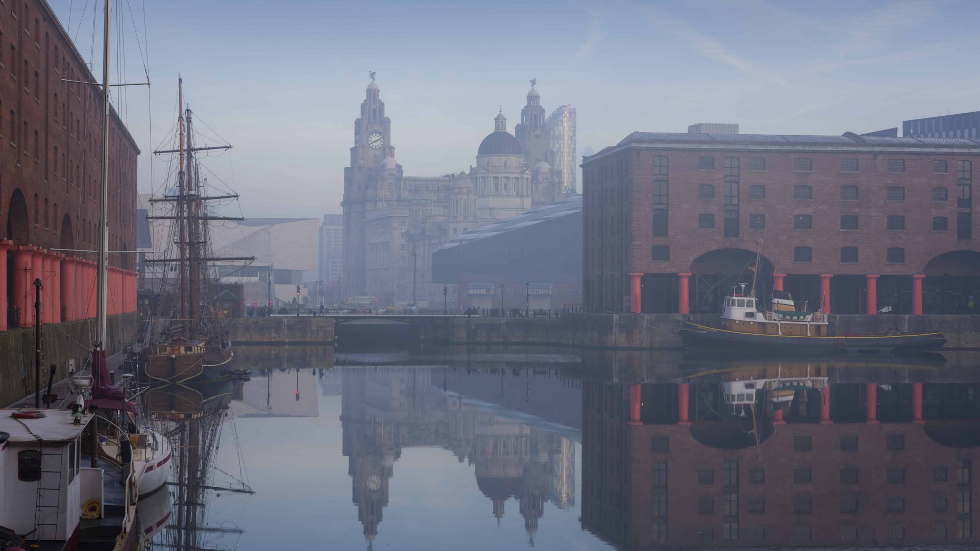 VB34133965 Maritime Albert Dock on Liverpool waterfront with the Three Graces historic buildings. The Liverpool world heritage site. Port of Liverpool building, the Cunard Building and the Liver building. A historic ship moored. Mist rising from the water.
