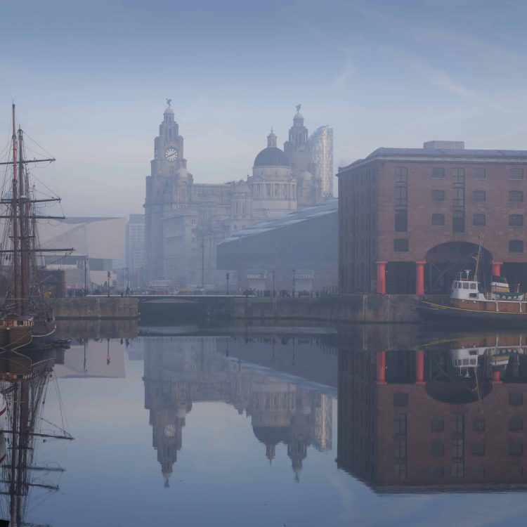 VB34133965 Maritime Albert Dock on Liverpool waterfront with the Three Graces historic buildings. The Liverpool world heritage site. Port of Liverpool building, the Cunard Building and the Liver building. A historic ship moored. Mist rising from the water.